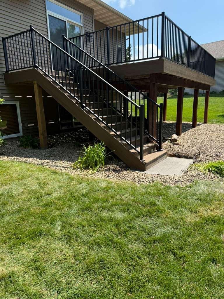 Elevated deck with a staircase and black metal railings down to the lawn
